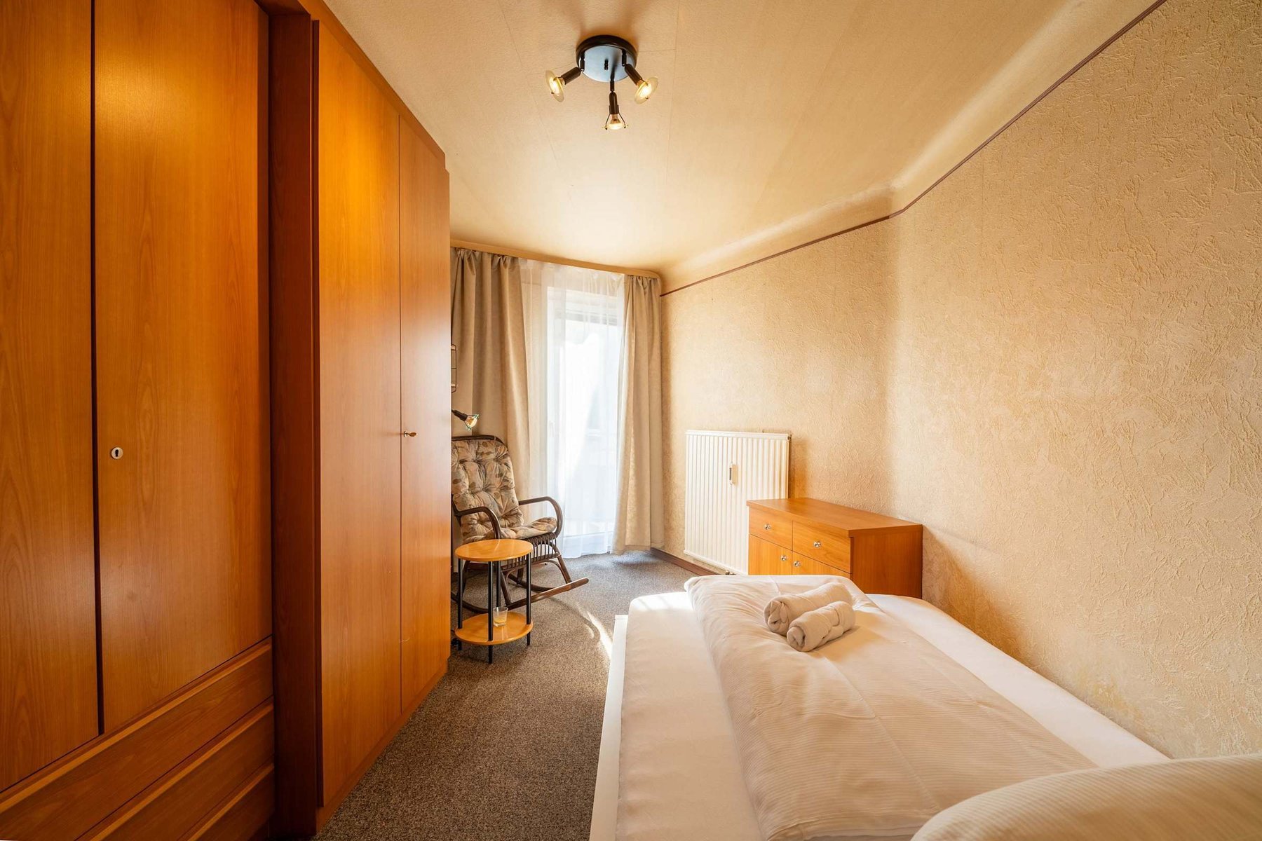 Second Bedroom in Natural Light - Spacious, Carpeted, with a Rocking Chair for Reading or Reflection