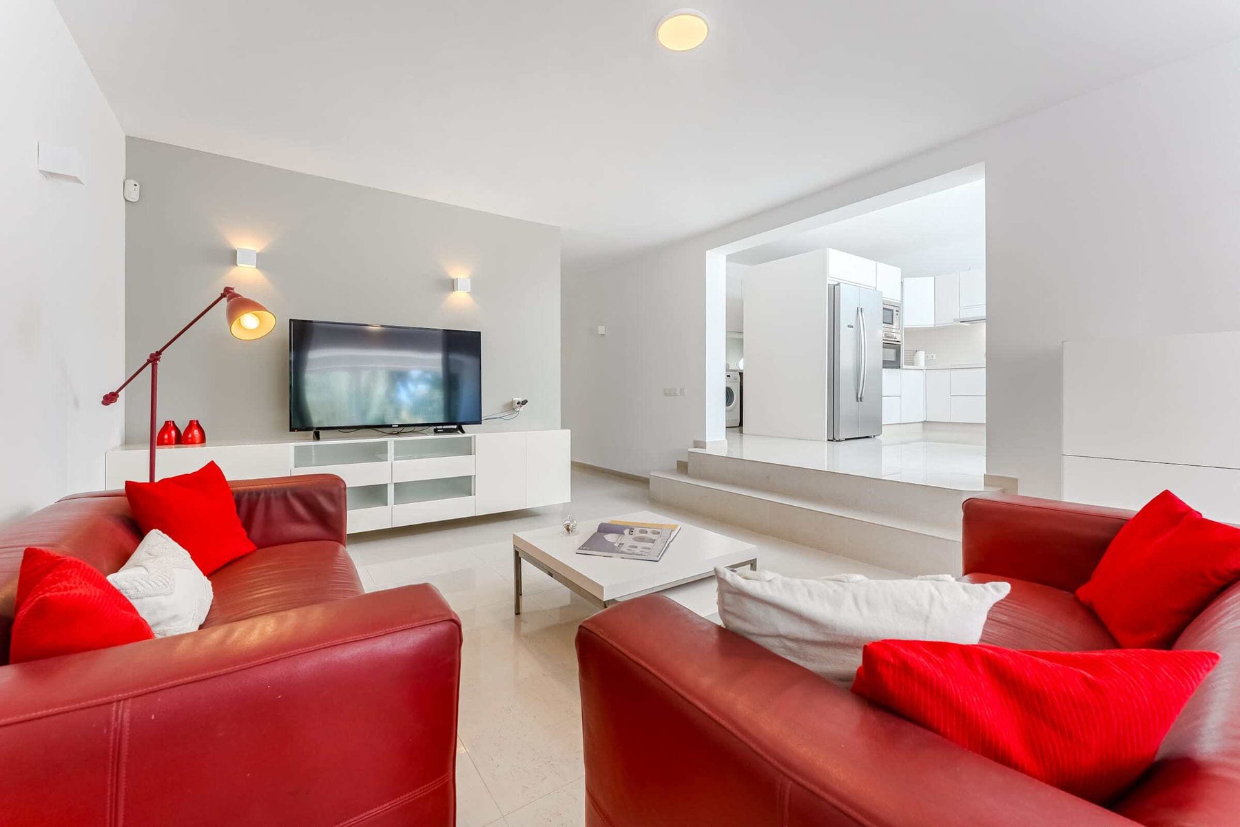 Lounge Area with Bold Red Sofas, Smart TV and Open Flow into Kitchen – Designed for Social Comfort