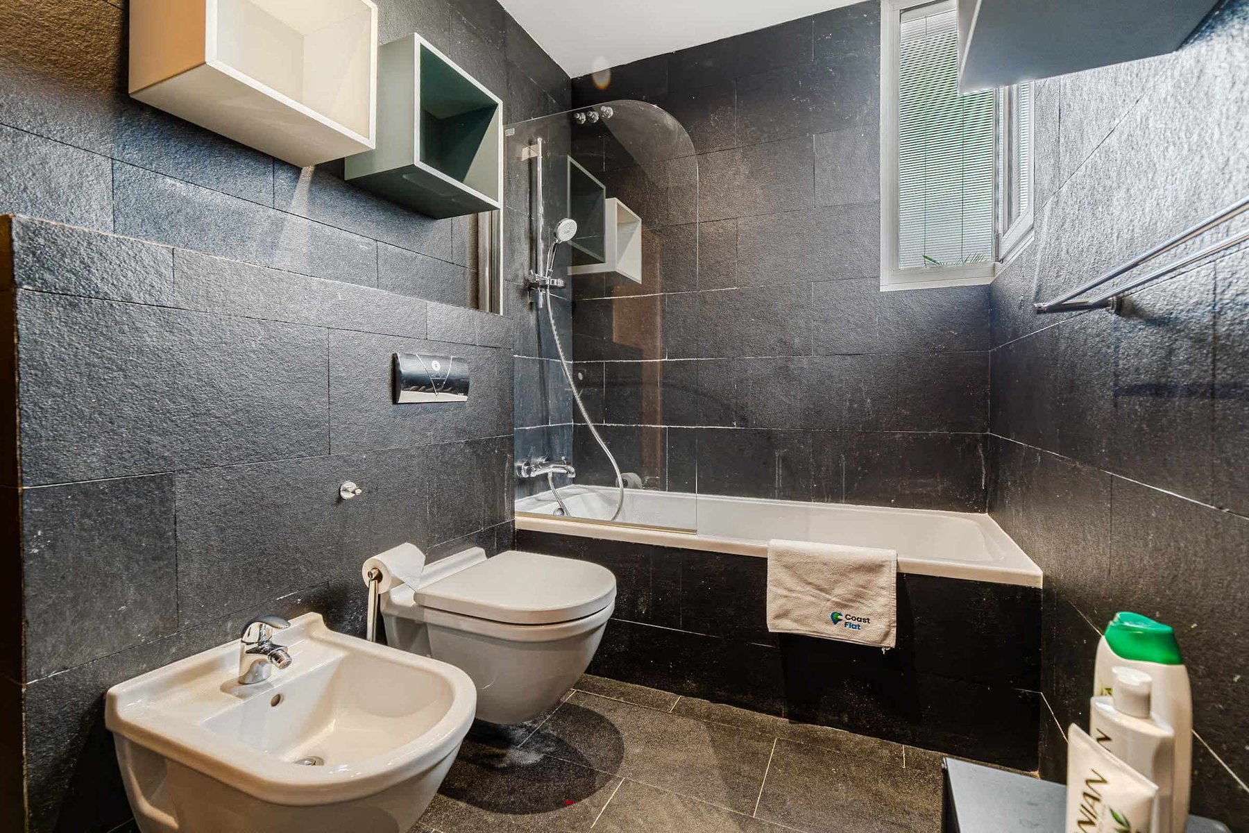 Stylish Black-Tiled Bathroom with Bathtub - Sleek Design and Natural Light